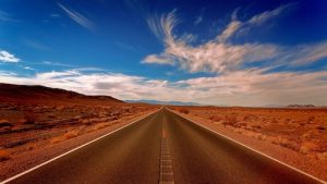 Long straight road through red desert with wispy clouds